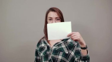 happy woman with glasses holds a white sheet of paper in hand, shows her thumb