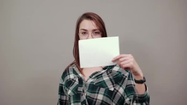 Mujer feliz con gafas sostiene una hoja blanca de papel en la mano, muestra su pulgar — Vídeos de Stock