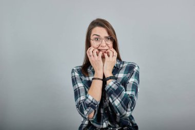 frightened woman with glasses is afraid, holds hands near mouth