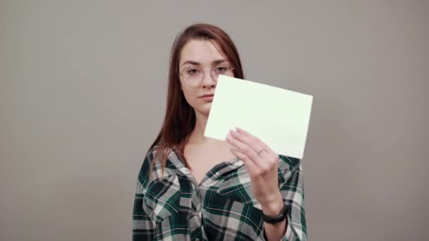 Mujer excitada sostiene una hoja blanca de papel en su mano, cruza los dedos — Vídeos de Stock