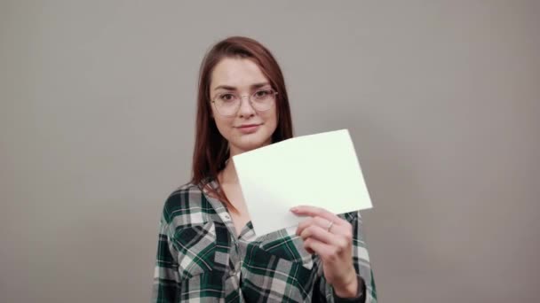 Mulher feliz com óculos segura uma folha branca de papel na mão, mostra seu polegar — Vídeo de Stock