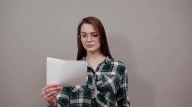 stylish woman in glasses holds a white sheet of paper in her hand