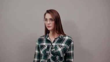 on grey background shocked woman in glasses points the direction