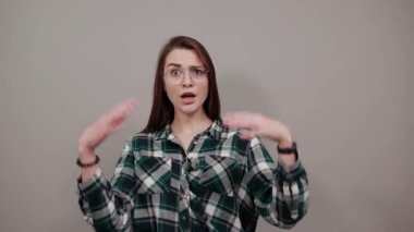 on grey background shocked woman spreads her hands