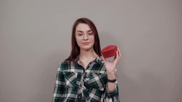 Gelukkig vrouw met bril houdt geschenk doos in de vorm van een rood hart in haar hand — Stockvideo