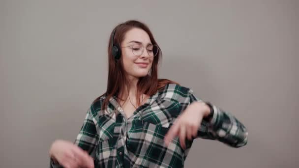 Happy woman in glasses listens to music in headphones, dancing moving hands — Stockvideo