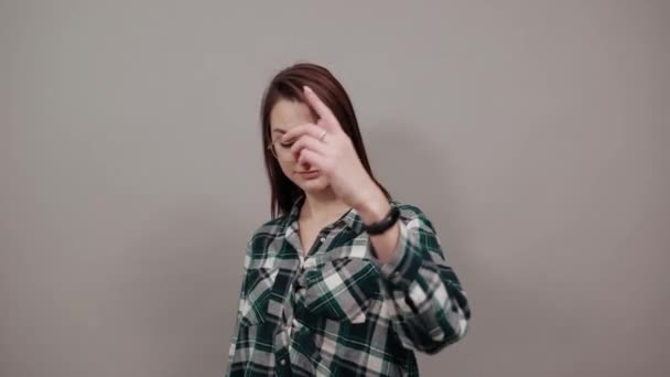 On grey background happy woman with glasses gestures with her fingers — Stockvideo