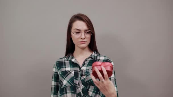 Mujer insatisfecha en gafas muestra regalo en forma de corazón rojo, parada gesto — Vídeos de Stock