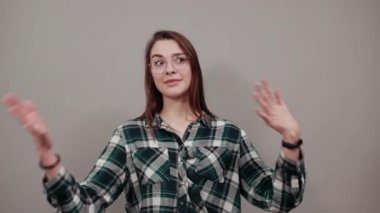 on grey background confident woman in glasses shows hands on herself