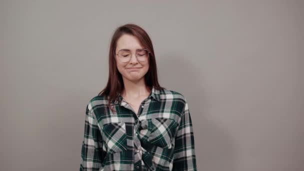 На сером фоне расстроена женщина в очках с плохим настроением — стоковое видео