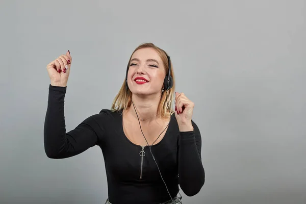 Menina de casaco preto mulher ouve música em um fone de ouvido dança, move as mãos — Fotografia de Stock