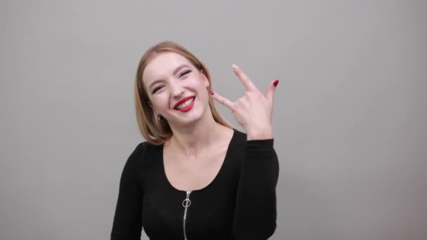 Fiatal szőke lány fekete kabátban boldog nő mutatja ujjak szimbóluma szikla — Stock videók