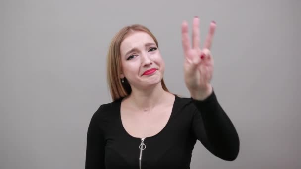 Girl in black jacket on grey background smiling woman shows three fingers — Stock Video