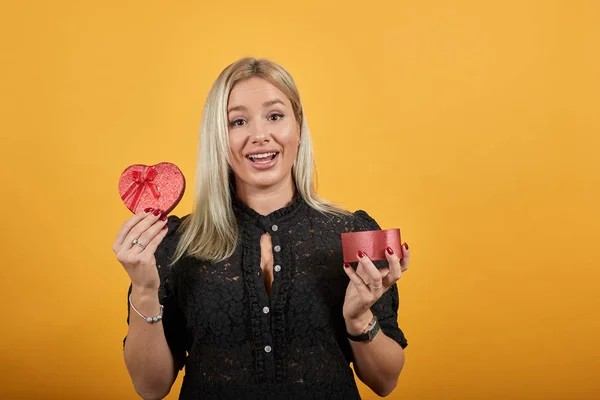 Chica en vestido negro mujer feliz muestra regalo sorpresa roja en forma de caja de corazón —  Fotos de Stock