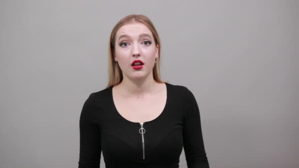 Joven chica rubia en chaqueta negra mujer conmocionada sostiene sus manos sobre sus mejillas — Vídeo de stock