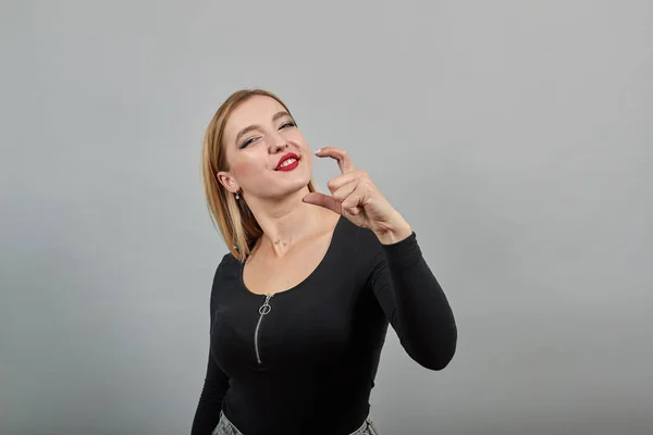 Young blonde girl in black jacket happy smiling woman shows size with fingers — 스톡 사진