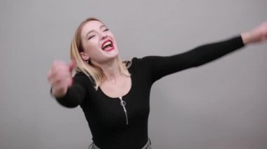 Young blonde girl in black jacket happy woman reacts with smile raises hands up