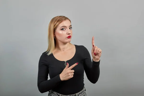 Girl in black jacket on grey background smart woman thinks, moves index fingers — Stock Fotó