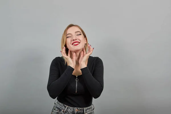 Blonde girl in black jacket happy woman touches her neck with fingers smiles — 图库照片