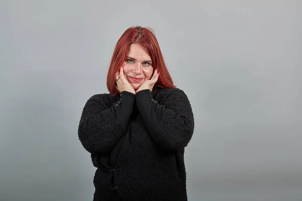 Young redhead fat lady in black sweater gentle woman touches her face with hands