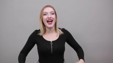 Young blonde girl in black jacket cheerful woman smiles points hands at herself