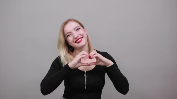 Joven chica rubia en chaqueta negra mujer linda muestra la forma del corazón con sus manos — Vídeos de Stock