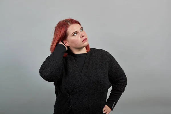 Young redhead fat lady in black sweater smart woman thinks, holds hand over head