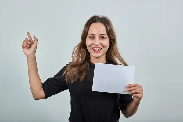 Frau mit einem weißen Blatt Papier in der Hand hebt Zeigefinger in die Höhe — Stockfoto