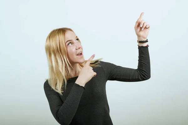 Em camisola preta em fundo branco, menina surpreendida mostra dedo indicador no objeto . — Fotografia de Stock