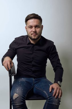 Kendine güvenen, ciddi bir adam. Sandalyeye oturuyor ve dik dik bakıyor..