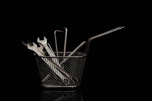Open-end wrenches and hex wrenches in a metal shopping basket on a black background.