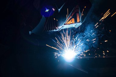 Tamamen karanlıkta maskeli bir kaynakçı metali kaynaklıyor..