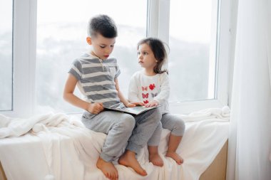 Erkek ve kız kardeş pencere kenarında oturuyorlar ve kitap okuyorlar. Mutluluk, aile