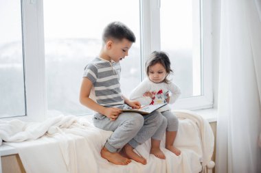 Erkek ve kız kardeş pencere kenarında oturuyorlar ve kitap okuyorlar. Mutluluk, aile