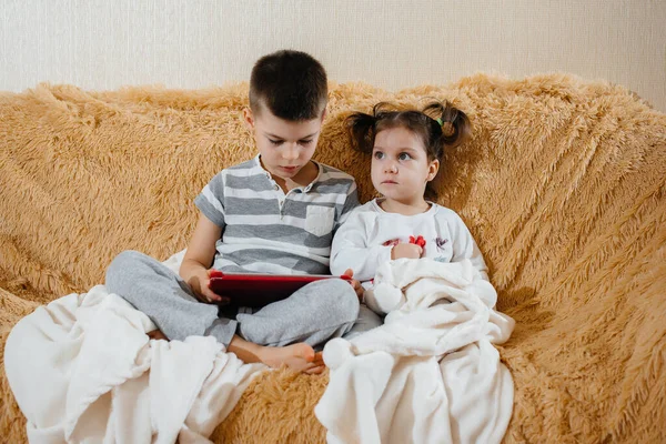 Brother and sister play on the couch in the tablet