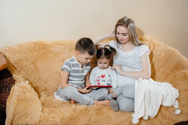 美しいです妊娠中のお母さん座っていますザソファとともに彼女の息子と娘とプレイタブレット — ストック写真