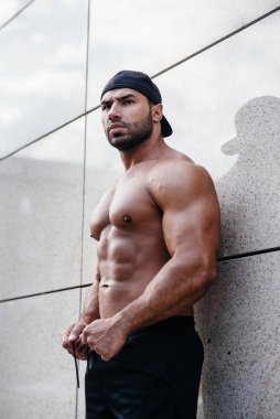 Seksi sporcu duvarın yanında üstsüz duruyor. Fitness, vücut geliştirme