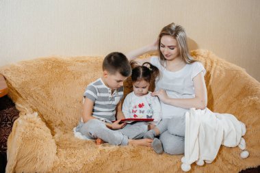 Güzel hamile anne oğlu ve kızıyla kanepede oturup tablet oynuyor.