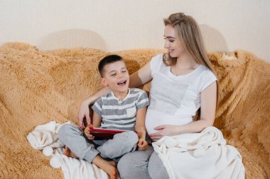 Hamile anne oğluyla tabletteki kanepede oynuyor. Dikkat, aile, sevgi