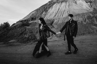 Siyah deri elbiseli Asyalı bir çift ağaçların arasında yürür. Siyah-beyaz