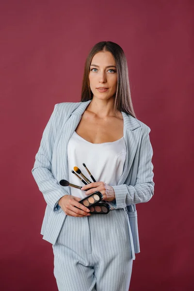 A beautiful young makeup artist poses in a suit with tassels on the background in the Studio. Makeup