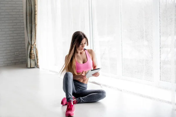 Sporty young girl counts calories on a tablet in the Studio on a light background. Fitness, healthy lifestyle