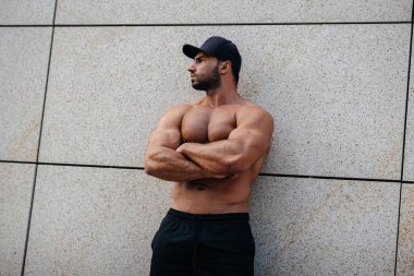 Seksi sporcu duvarın yanında üstsüz duruyor. Fitness, vücut geliştirme
