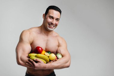 Parlak meyveli beyaz bir arka planda poz veren sportif seksi adam. Diyet olsun. Sağlıklı beslenme