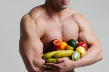 Parlak meyveli beyaz bir arka planda poz veren sportif seksi adam. Diyet olsun. Sağlıklı beslenme