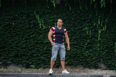 Sportif bir adam yeşil bir bitki duvarının yanında oturuyor. Ekoloji