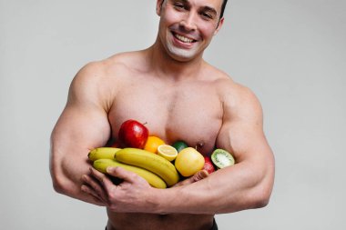 Parlak meyveli beyaz bir arka planda poz veren sportif seksi adam. Diyet olsun. Sağlıklı beslenme