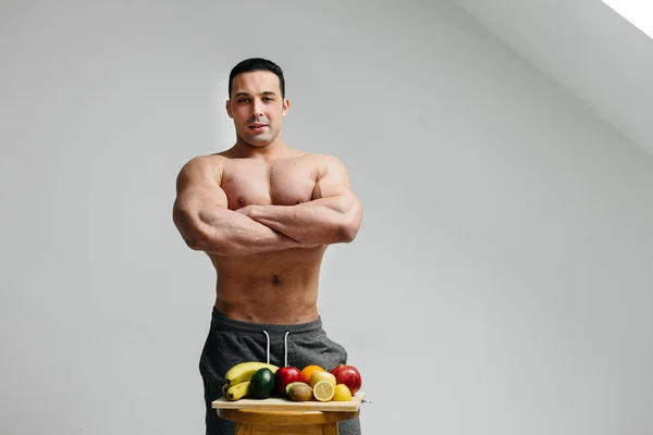 Sexy vegan guy with a naked torso posing in the Studio next to fruit. Diet. Healthy diet
