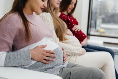 Hamile kızlar göbeklerini elleriyle yakın plan çekimde tutarlar. Hamile kızların doğum öncesi sınıfı.