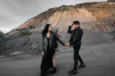 Siyah deri elbiseli Asyalı bir çift ağaçların arasında yürür. Tarz, moda, aşk